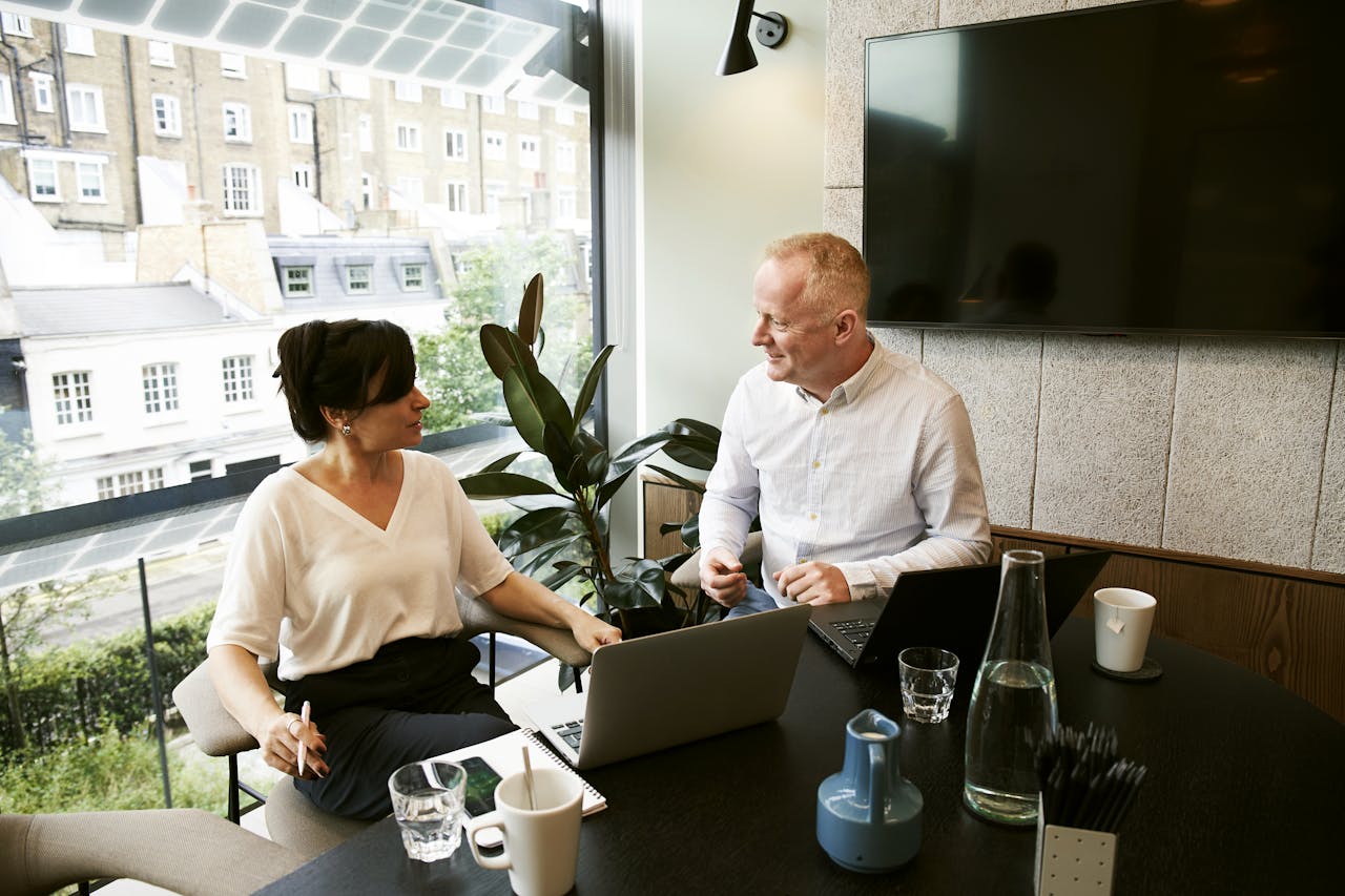 Services Two business professionals engaging in a team meeting in a modern London office with a large window view.